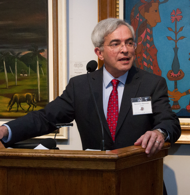 there is a man in a suit and tie standing at a podium in front of a painting